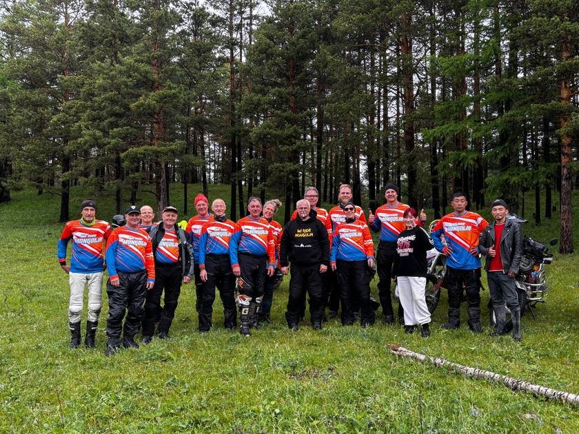Riders in matching We Ride Mongolia jerseys gathered in the pine forest