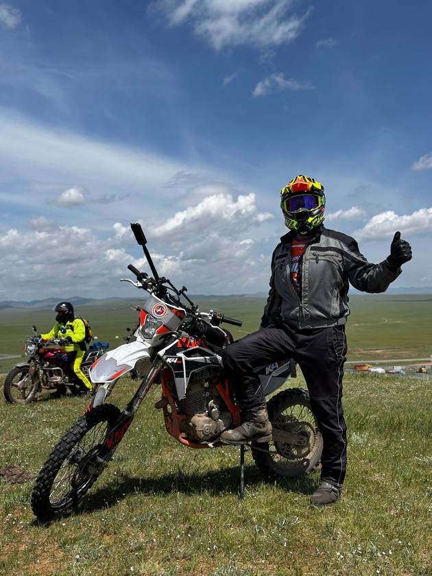 Rider giving a thumbs up beside his dirt bike on the steppe
