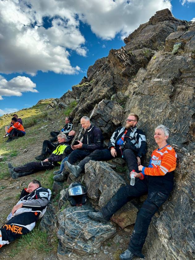 Riders resting against a rock face during a break