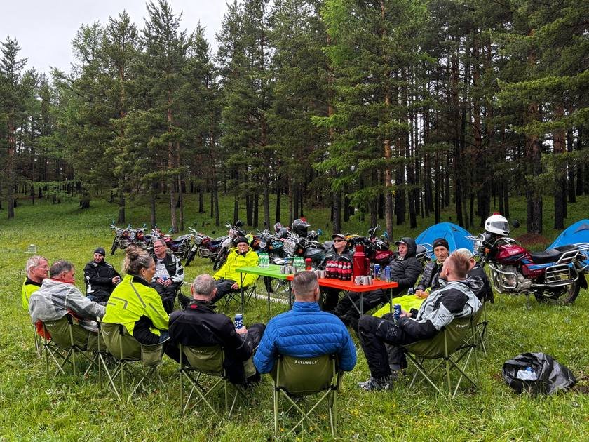 Riders sharing drinks around a camp table in the forest