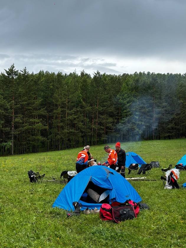 Blue tents and a campfire in a forest meadow