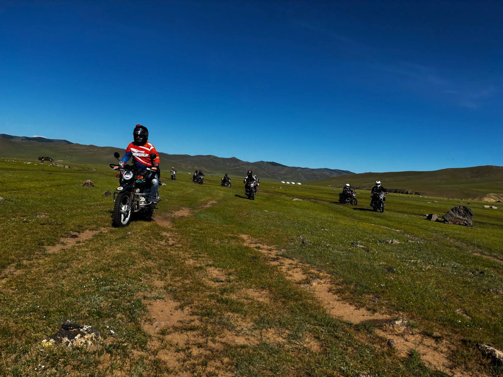 Riders crossing the green Mongolian steppe under a deep blue sky